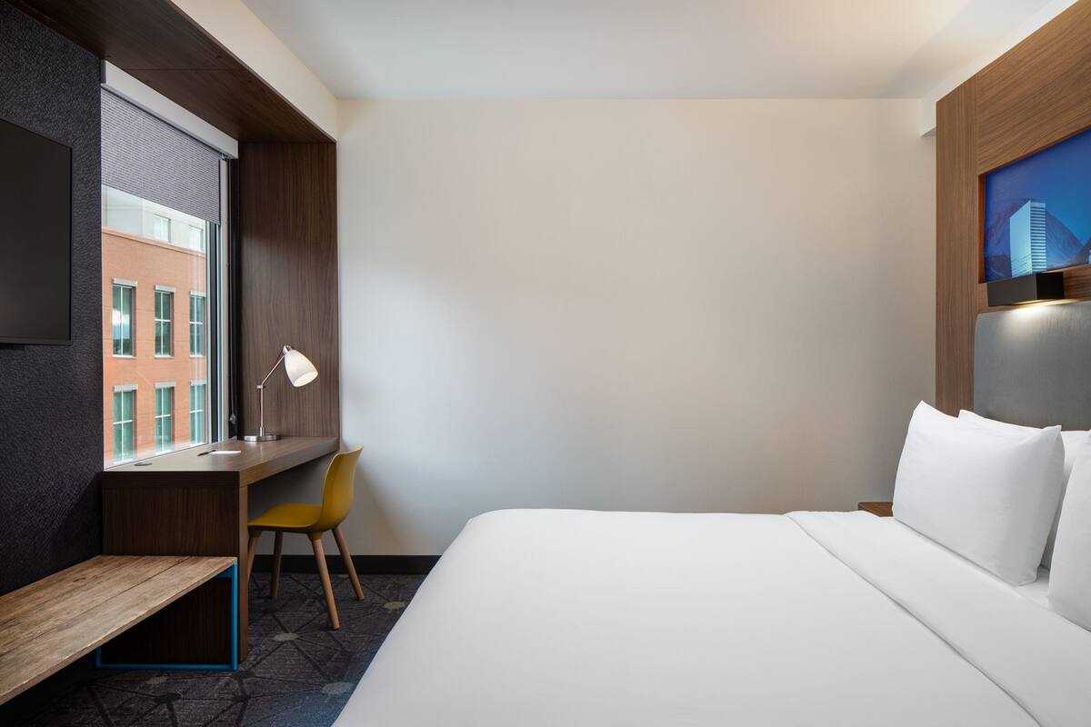 Una habitación de hotel con una cama, un escritorio con una silla, un televisor y una ventana con persianas.