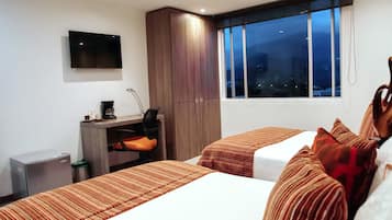 A hotel room with two beds, a desk with a chair, a TV, and a window with a city view.