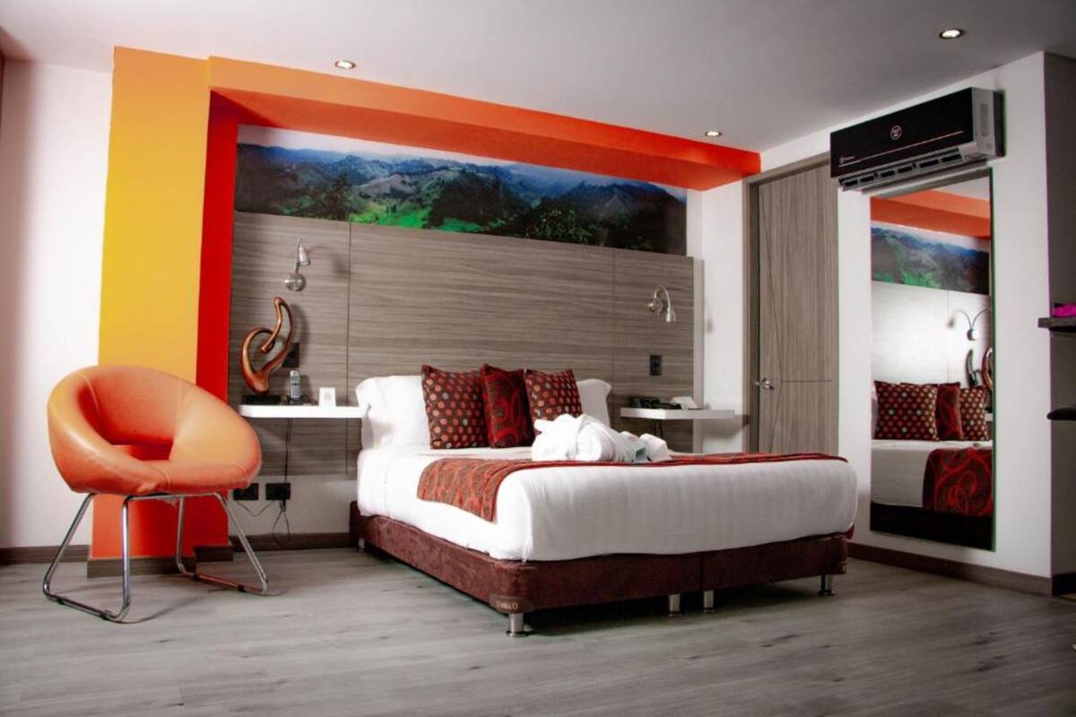 A modern hotel room with a bed, a chair, a nightstand, and a large window with a mountain view.