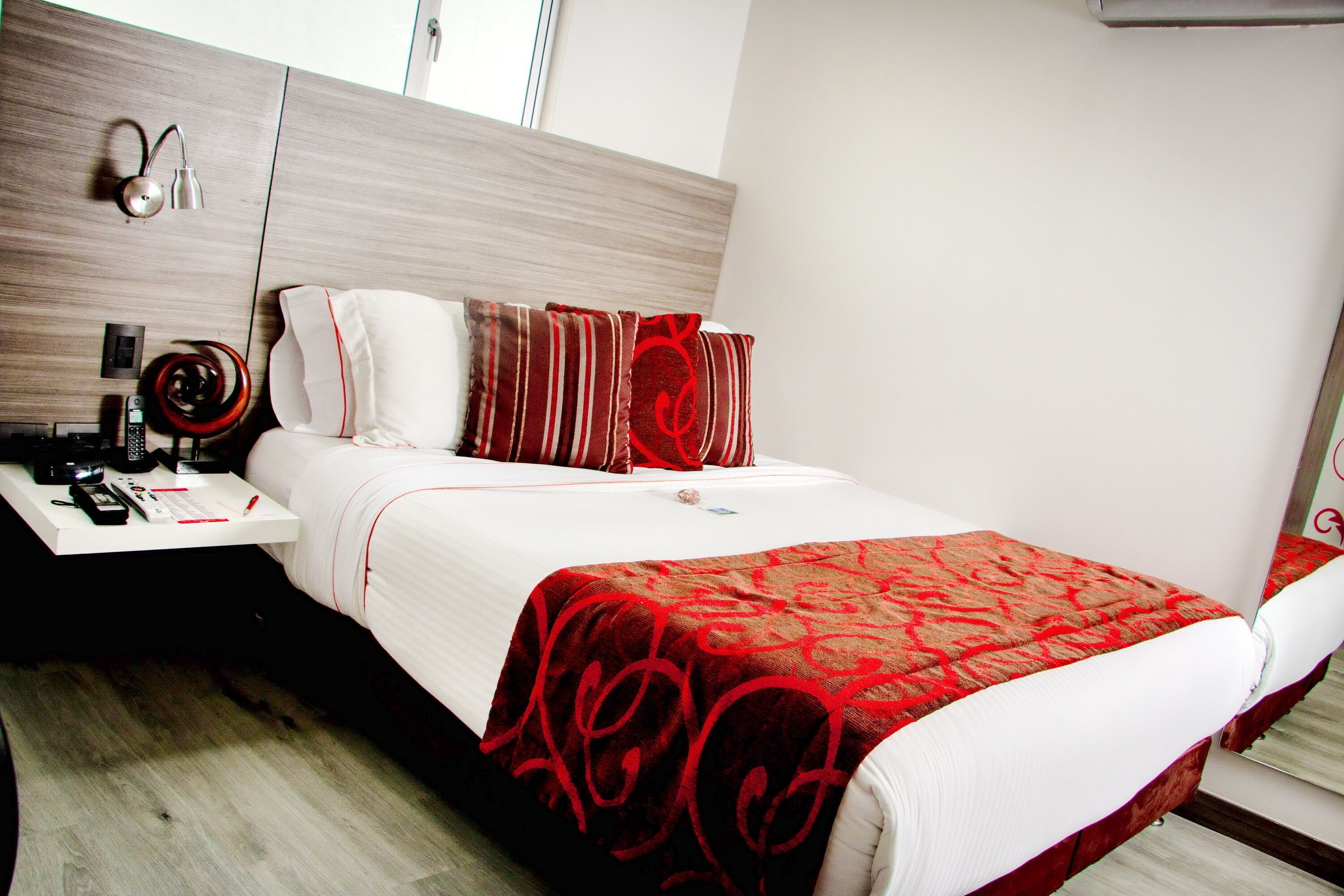 Quarto de hotel com cama, mesa de cabeceira, abajur e espelho.