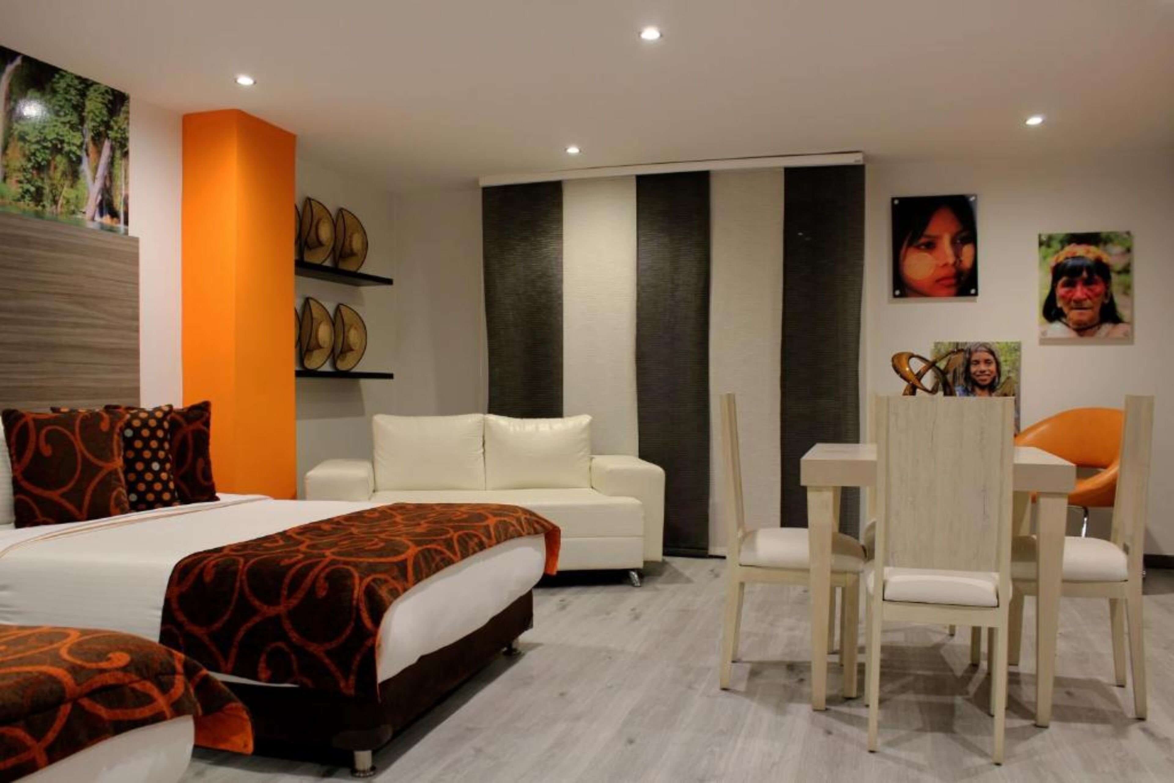 Een moderne hotelkamer met een groot bed, een witte bank, een eettafel met stoelen en kunstwerken aan de muur.