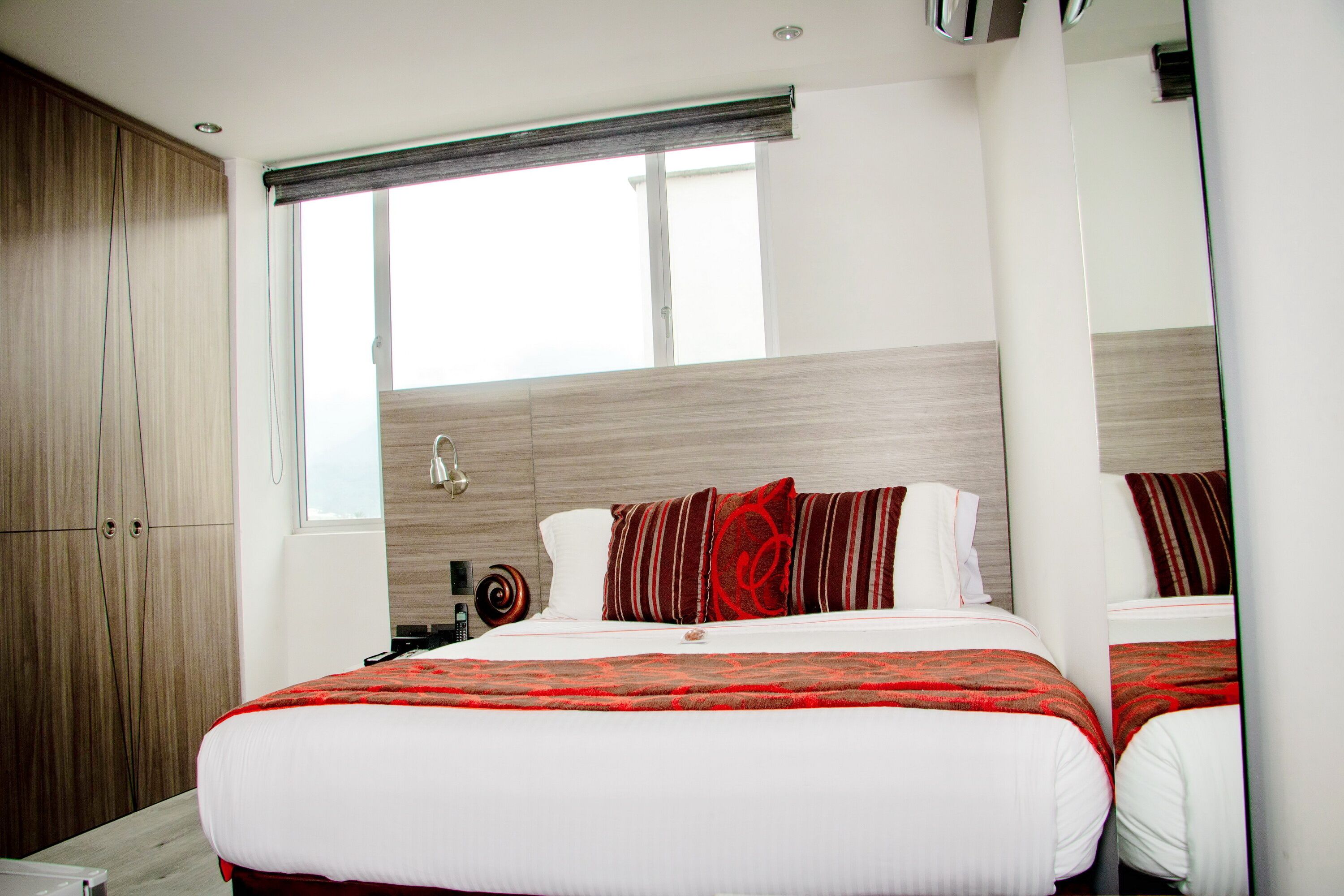 A modern hotel room with a large bed, a wardrobe, and a window with blinds.