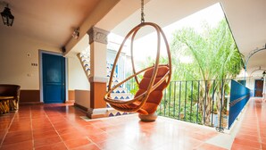 Una silla colgante en una habitación iluminada por el sol, con vistas a un jardín y una puerta azul.