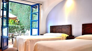 Una habitación con dos camas, un cabecero de madera y vistas a la vegetación a través de una puerta abierta.