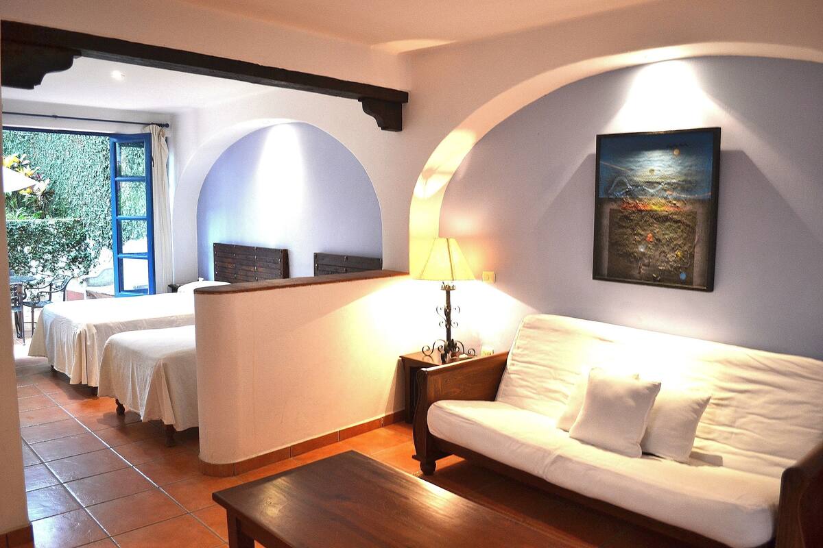 Una habitación de hotel con cama, sofá, lámpara y un cuadro en la pared.