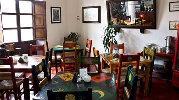 A restaurant interior with wooden tables and chairs, framed pictures on the walls, and a large mirror reflecting the room.