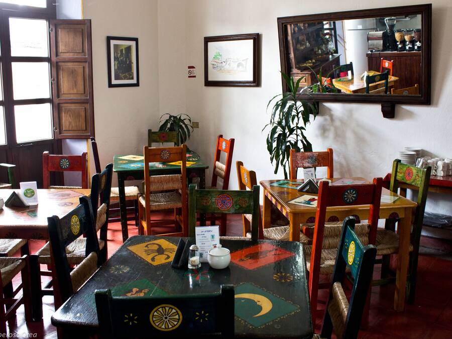 A restaurant interior with wooden tables and chairs, framed pictures on the walls, and a large mirror reflecting the room.