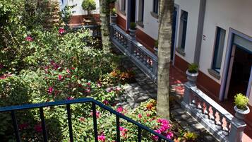 Un patio con balcón, plantas en macetas y vistas a un edificio con múltiples ventanas y puertas.