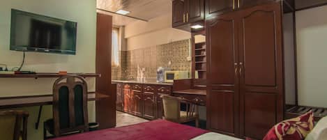 A hotel room with a bed, a desk, a TV, and a kitchenette.