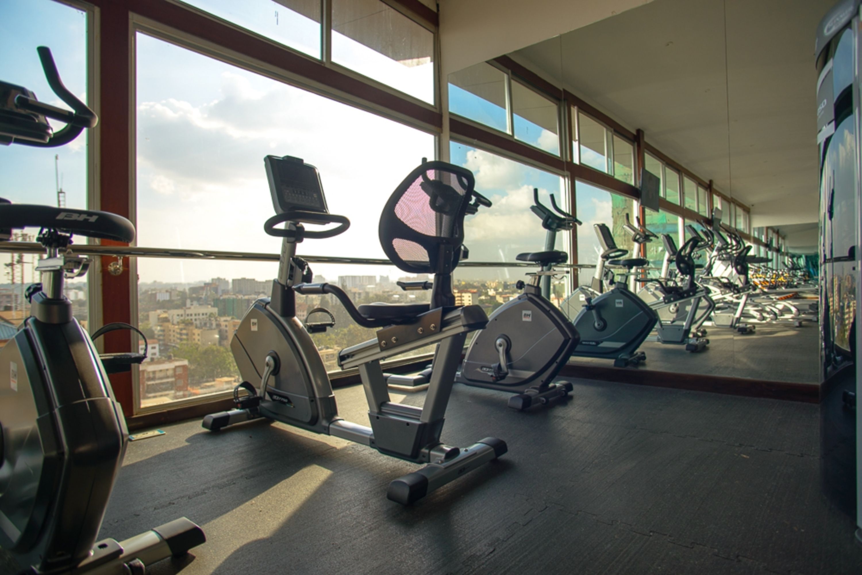 A gym with various exercise equipment, large windows, and a view of the cityscape.
