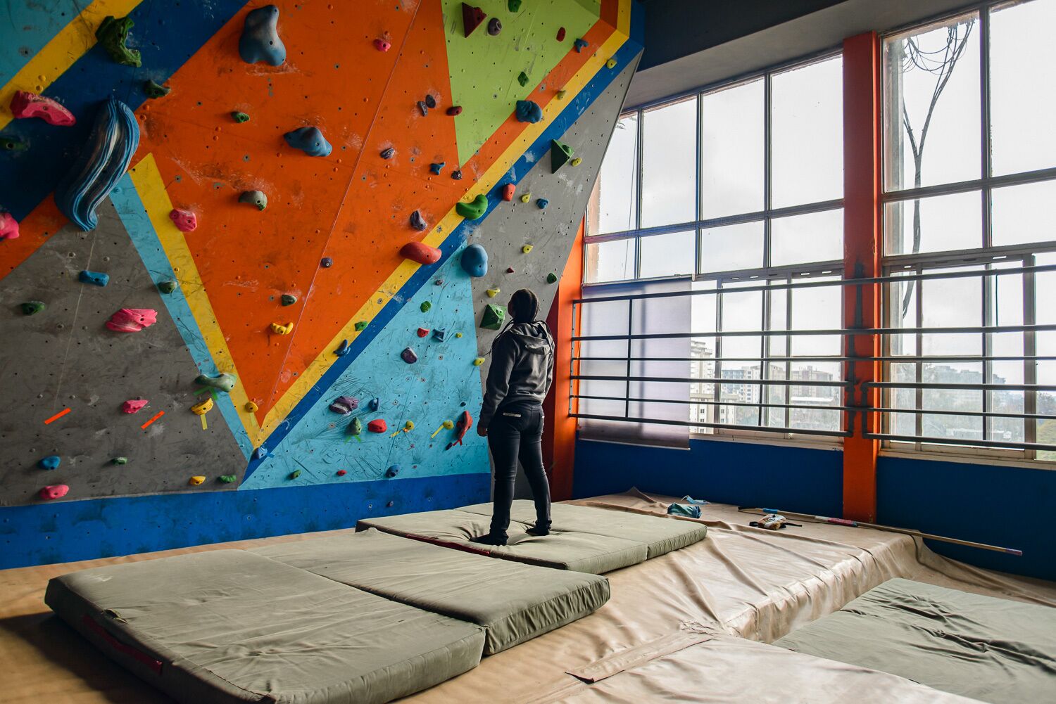 A climbing gym with a large climbing wall, padded flooring, and large windows.