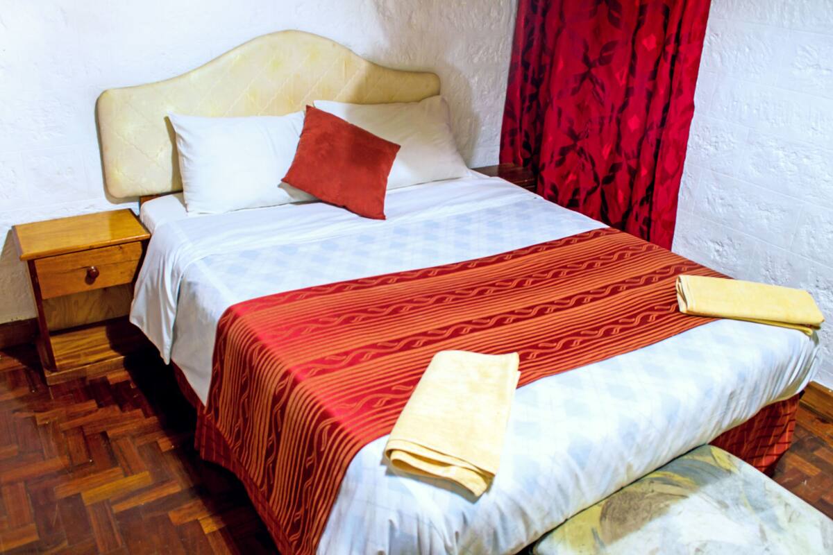 A bed with a patterned bedspread, pillows, and a folded towel.