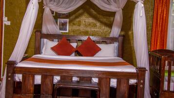 A wooden four-poster bed with white and orange bedding, two red pillows, and a small wooden bench at the foot of the bed.
