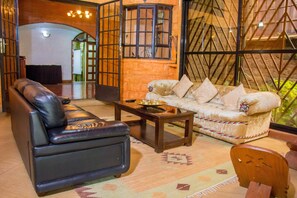 A living room with a leather sofa, a patterned rug, a wooden coffee table, and a white sofa with patterned cushions. - Bush House and Camp (Nairobi)