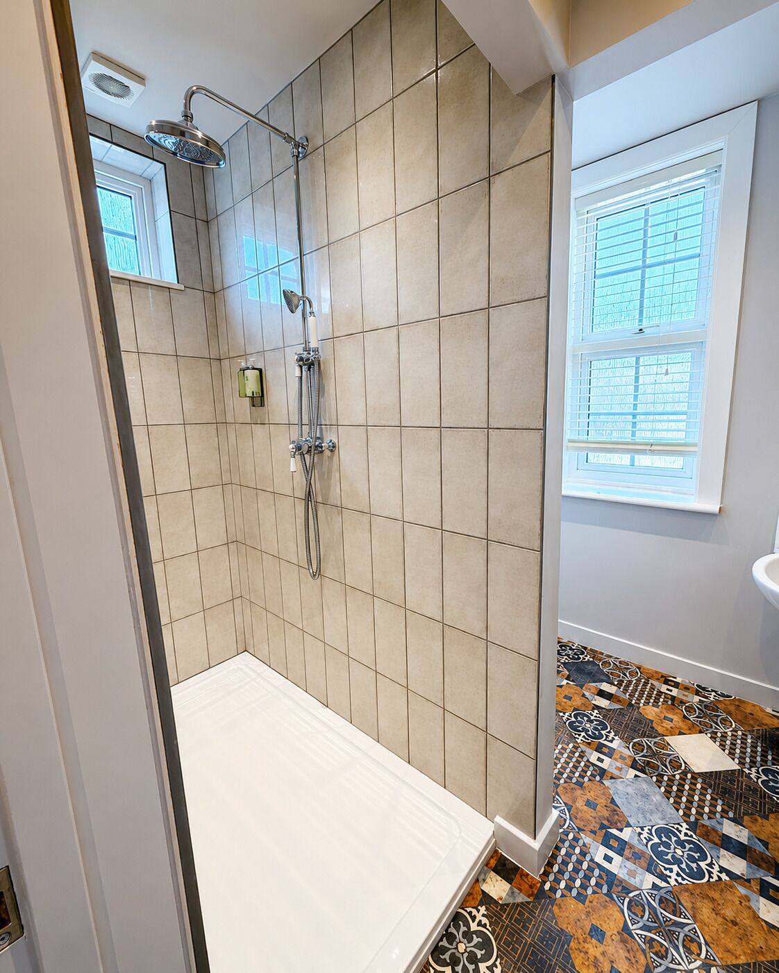 Een badkamer met een douche, betegelde wanden, een raam en een vloer met patroon.