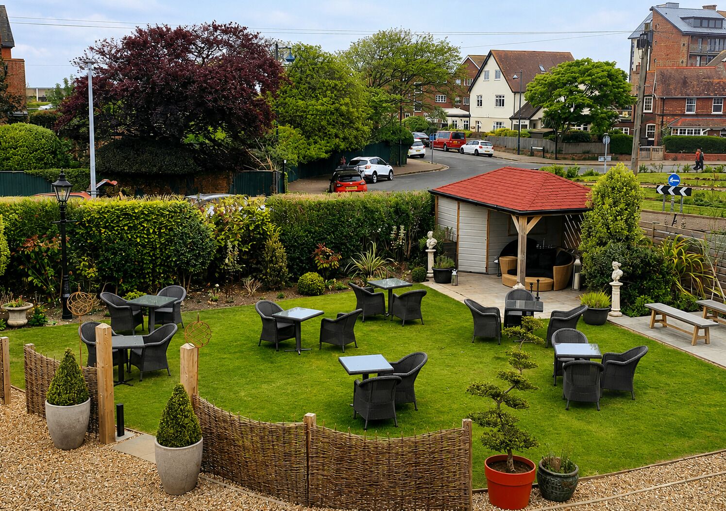 A patio area with outdoor seating, a small building with a red roof, and a hedge.