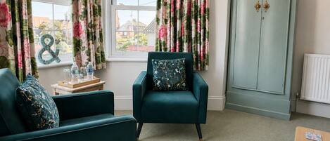 A room with teal armchairs, a wooden side table with water bottles, a radiator, and a wardrobe.