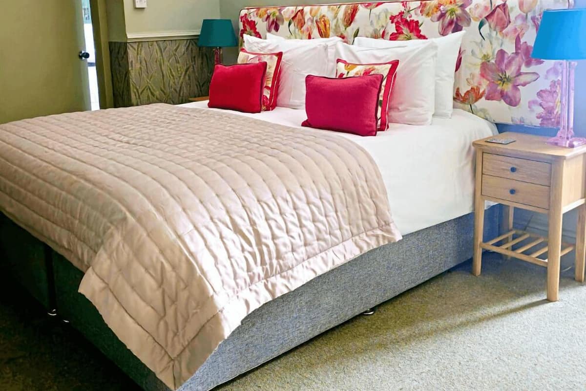 A neatly made bed with a floral headboard, two bedside tables with lamps, and a chandelier.