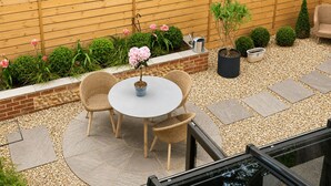 A patio with a round table and chairs, surrounded by a wooden fence, and a brick wall with a window. - Burlington Berties (Sheringham)