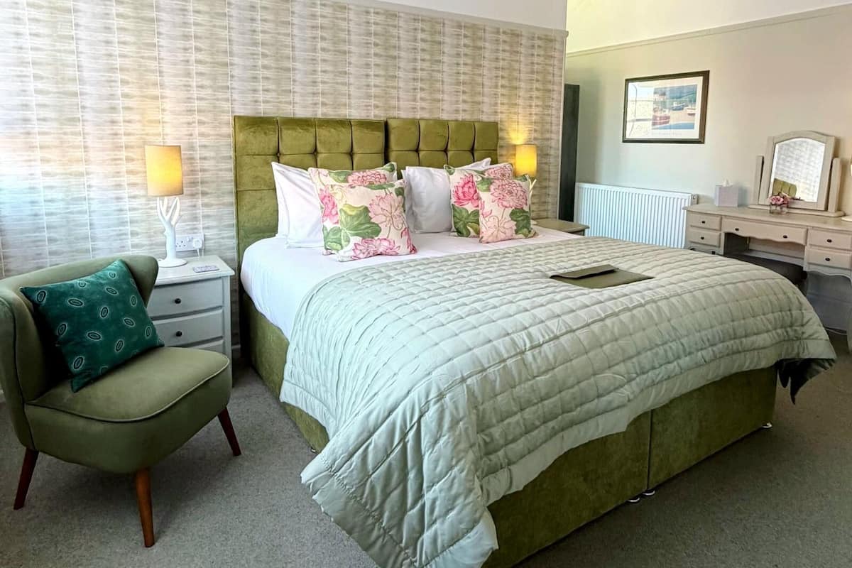 A bedroom with a large bed, a chair, a desk, and a radiator.