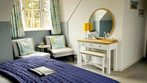 A bedroom with a bed, a desk, a chair, a window with curtains, a mirror, and a lamp. - Burlington Berties (Sheringham)
