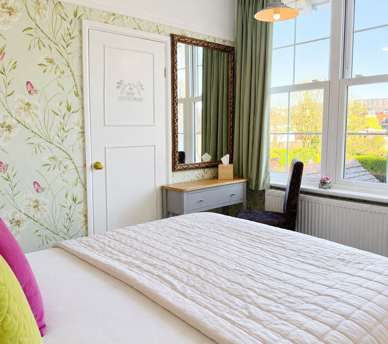 A bedroom with a bed, a dresser, a mirror, a chair, and a window with a view of greenery.