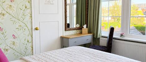A bedroom with a bed, a dresser, a mirror, a chair, and a window with a view of greenery.