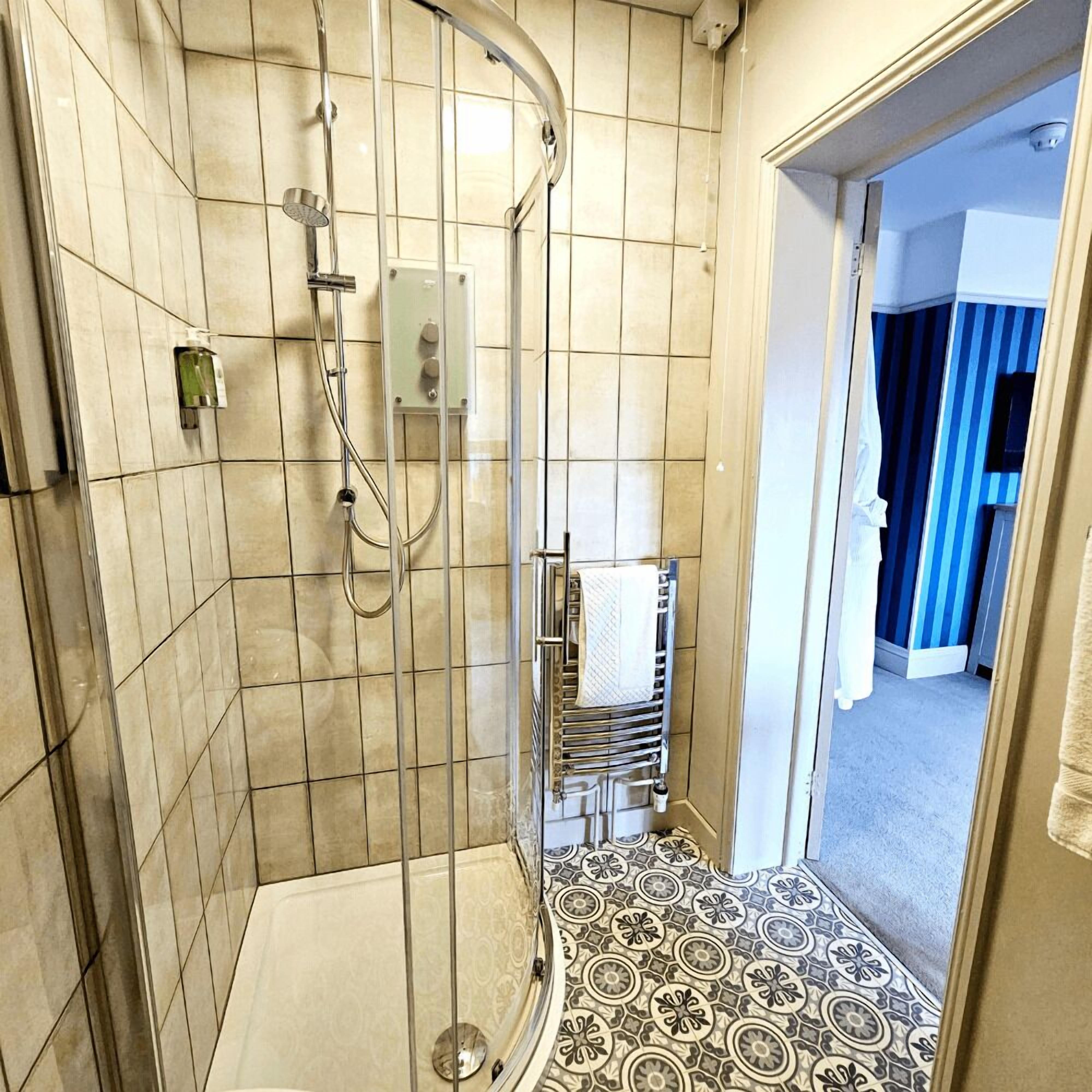 Une douche avec une porte en verre, un porte-serviettes et un carrelage décoratif.