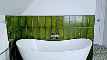 A modern bathroom with a freestanding bathtub, green tiled walls, and patterned floor tiles.