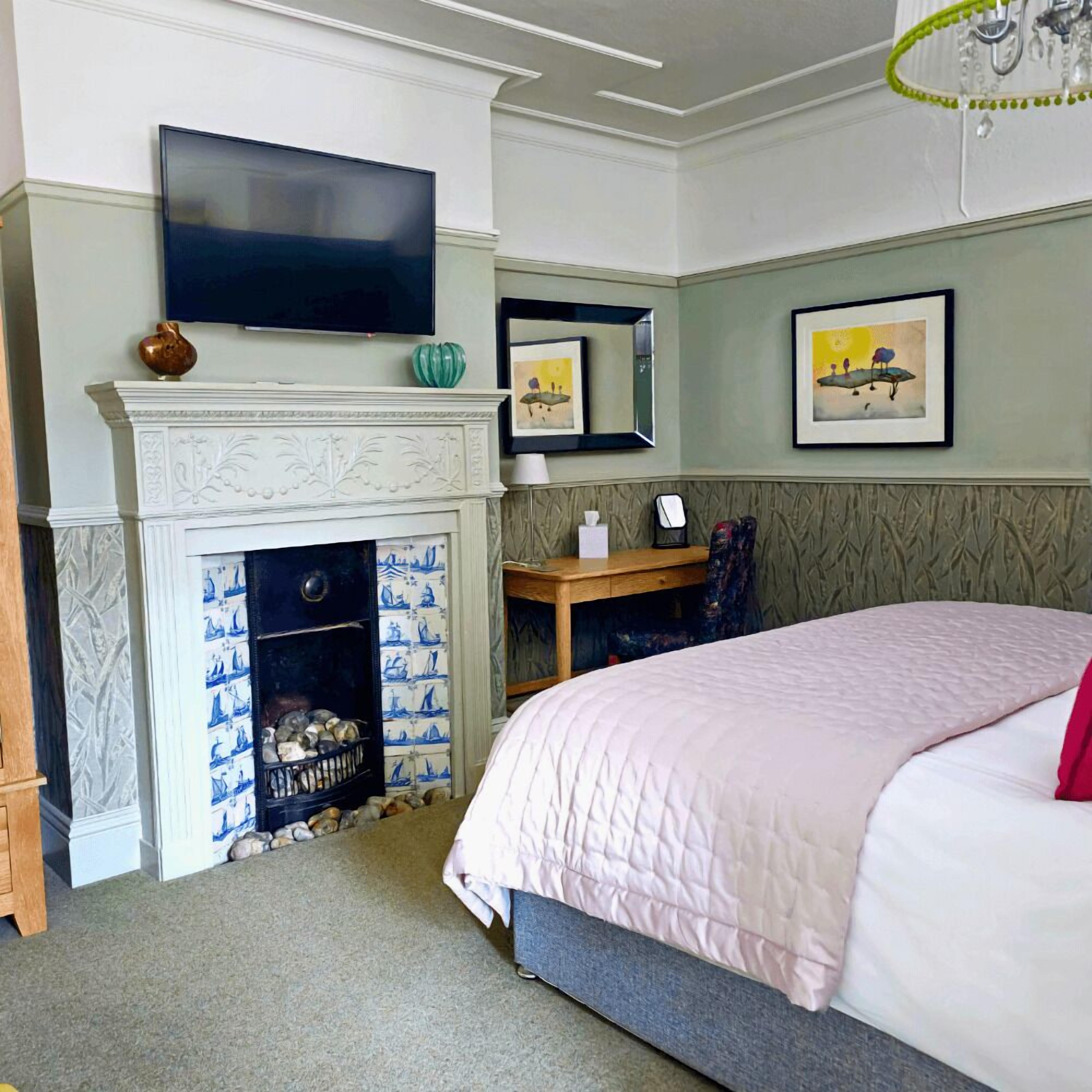 A bedroom with a bed, a fireplace, a television, and artwork on the walls.