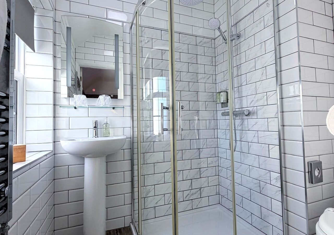 Un baño con baldosas de mármol blanco, cabina de ducha de vidrio, lavamanos y espejo.