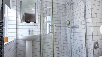 Un baño con baldosas de mármol blanco, cabina de ducha de vidrio, lavamanos y espejo.