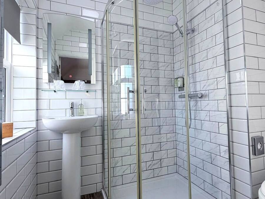 Un baño con baldosas de mármol blanco, cabina de ducha de vidrio, lavamanos y espejo.