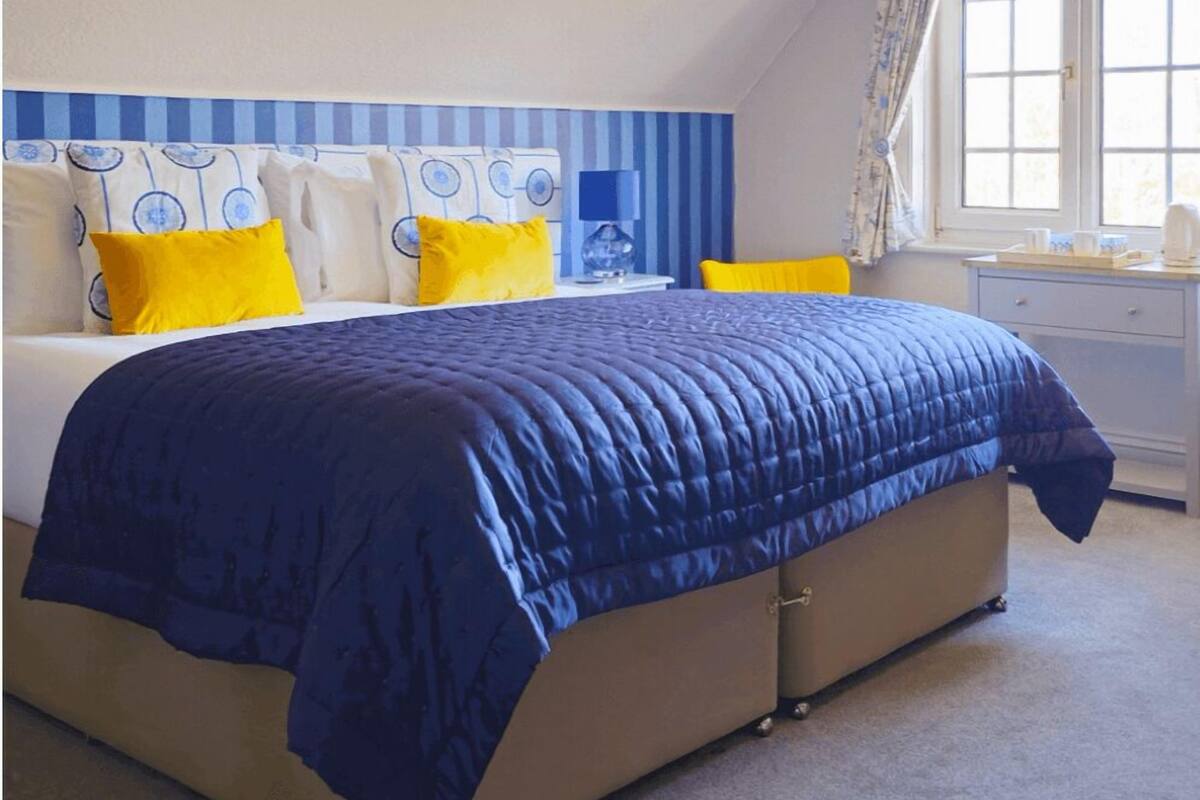 A bedroom with a bed, a nightstand, a window with curtains, and a wall with a striped pattern.