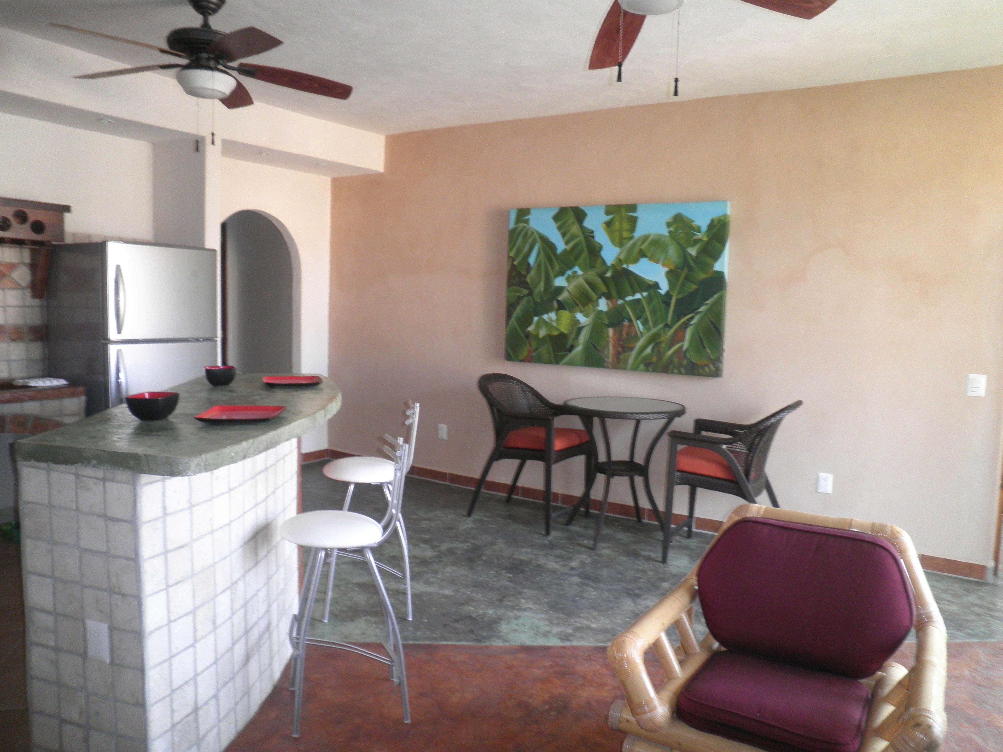 A kitchen with a refrigerator, a dining area with chairs and a table, and a ceiling fan.