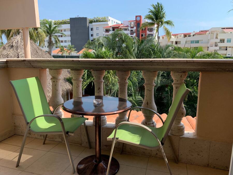 A balcony with a round table and two chairs, overlooking a residential area with buildings and palm trees.