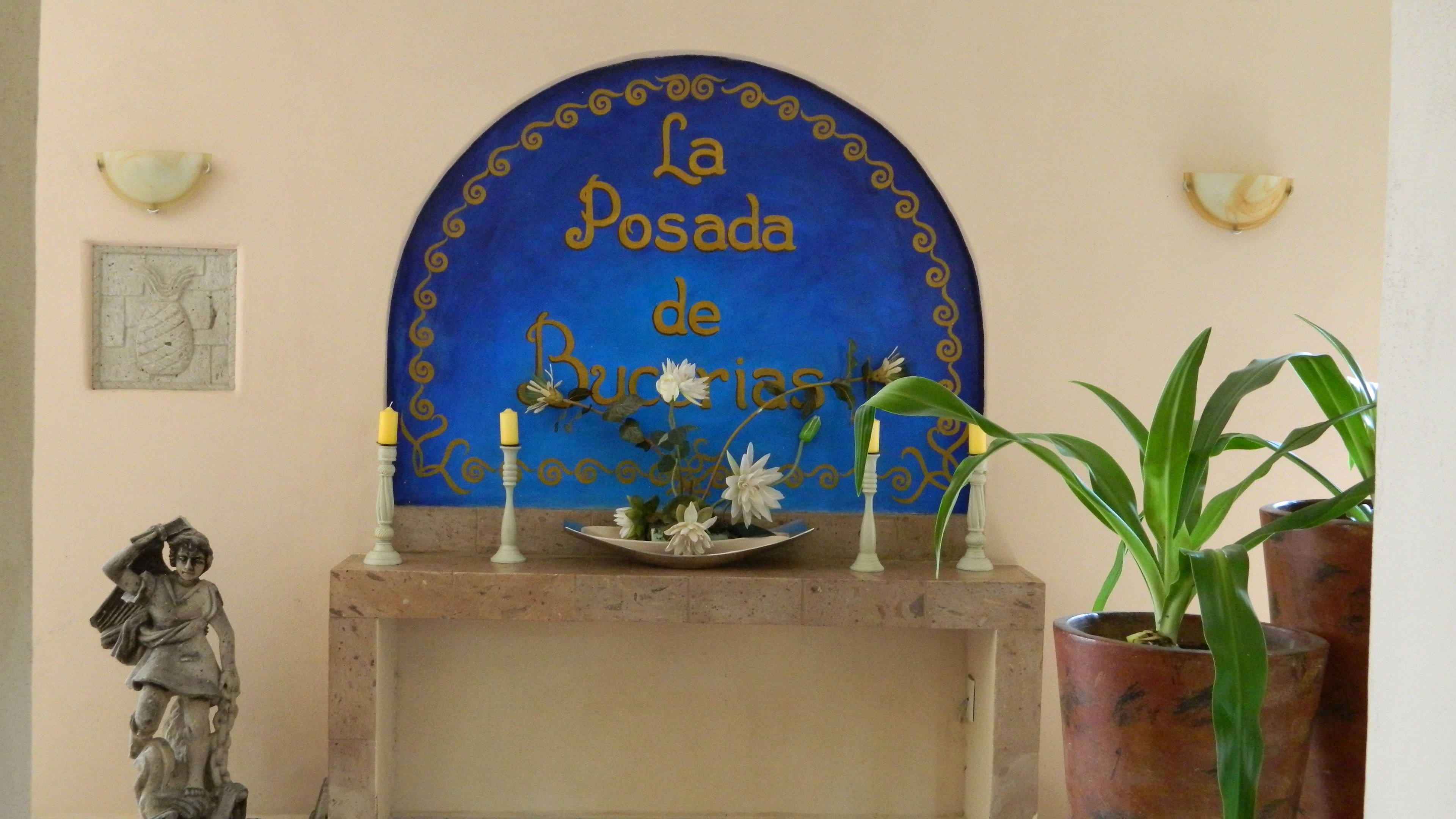 Un arc blau amb lletra daurada, una estàtua, una planta en test i un suport de vela amb espelmes.