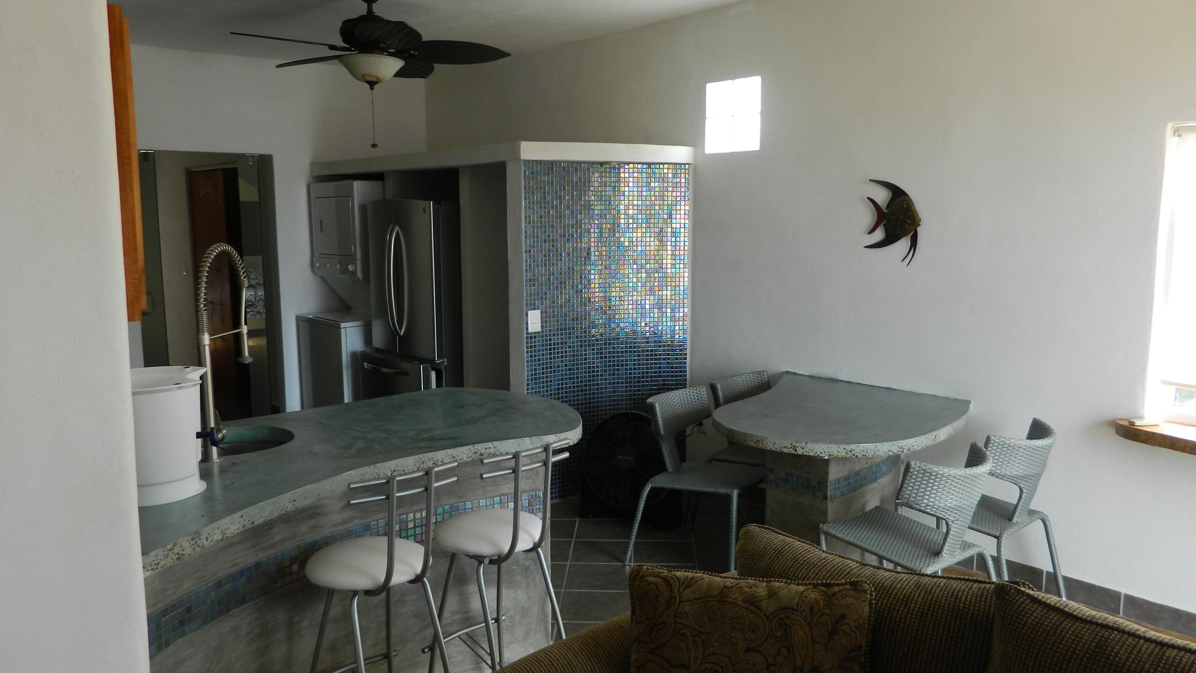 A compact kitchen with a bar area, a ceiling fan, and a decorative fish wall art piece.