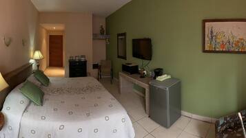 A hotel room with a bed, bedside lamp, desk, TV, and a painting on the wall.