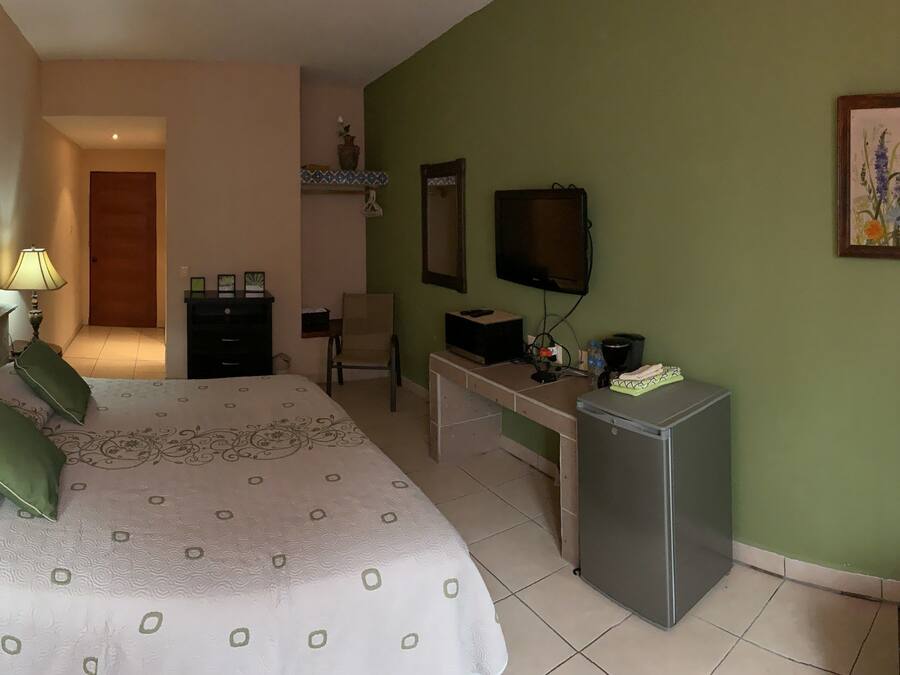 A hotel room with a bed, bedside lamp, desk, TV, and a painting on the wall.