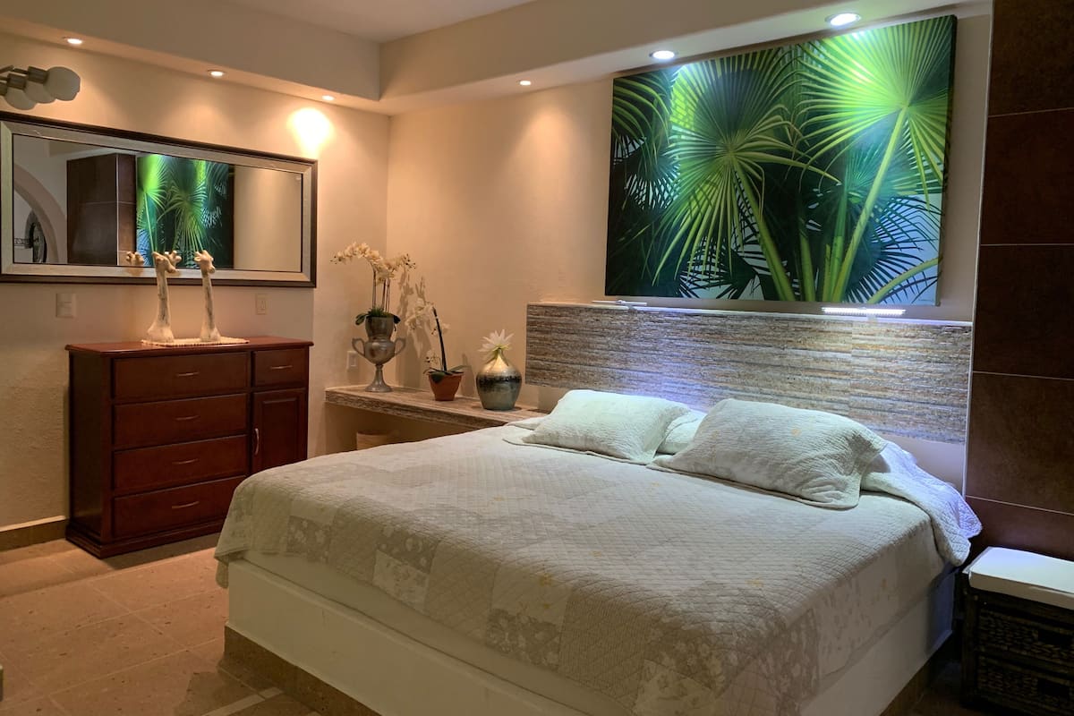 Une chambre à coucher comprenant un lit, une commode, un miroir et un luminaire fixé au mur.