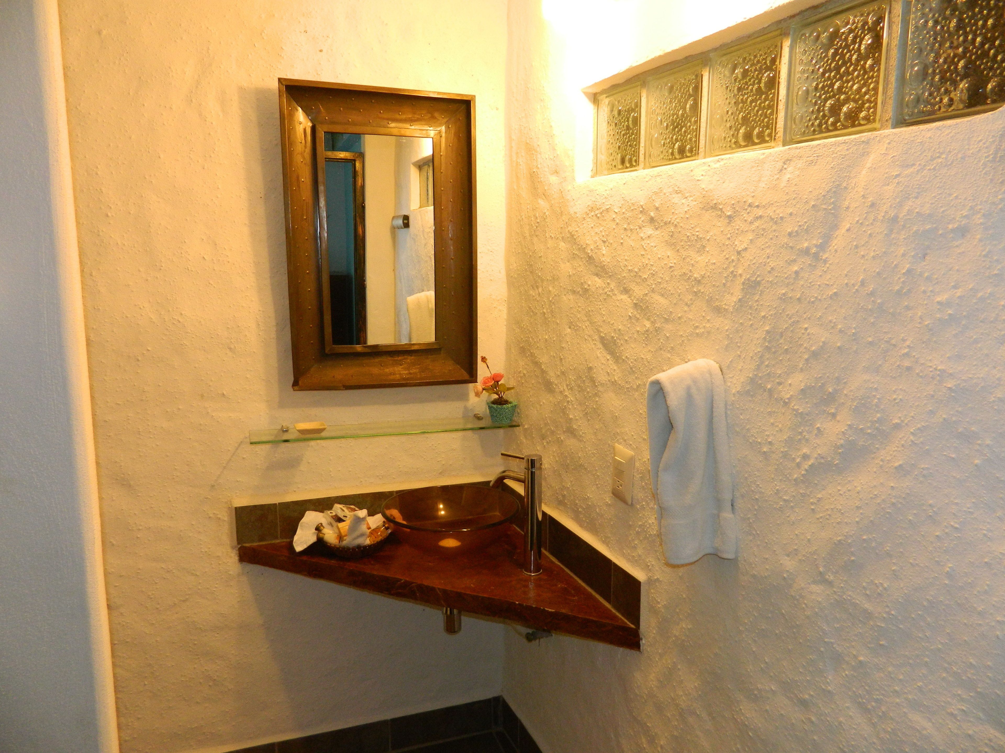 Une salle de bain équipée d’un lavabo, d’un miroir, d’un porte-serviettes et d’une étagère en verre.