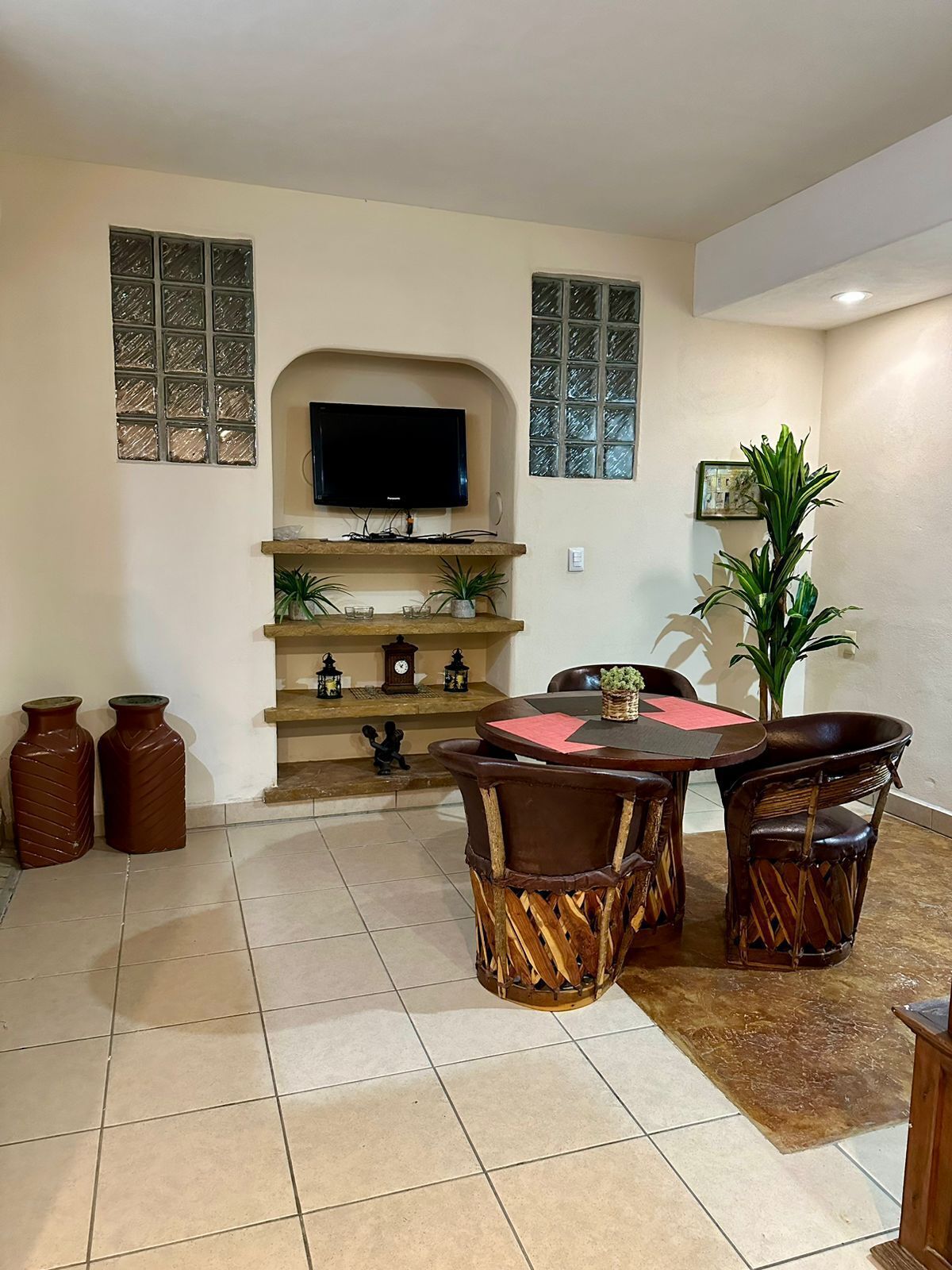 Un salon avec un téléviseur fixé au mur, une table à manger avec des chaises et une cheminée agrémentée d’objets décoratifs.