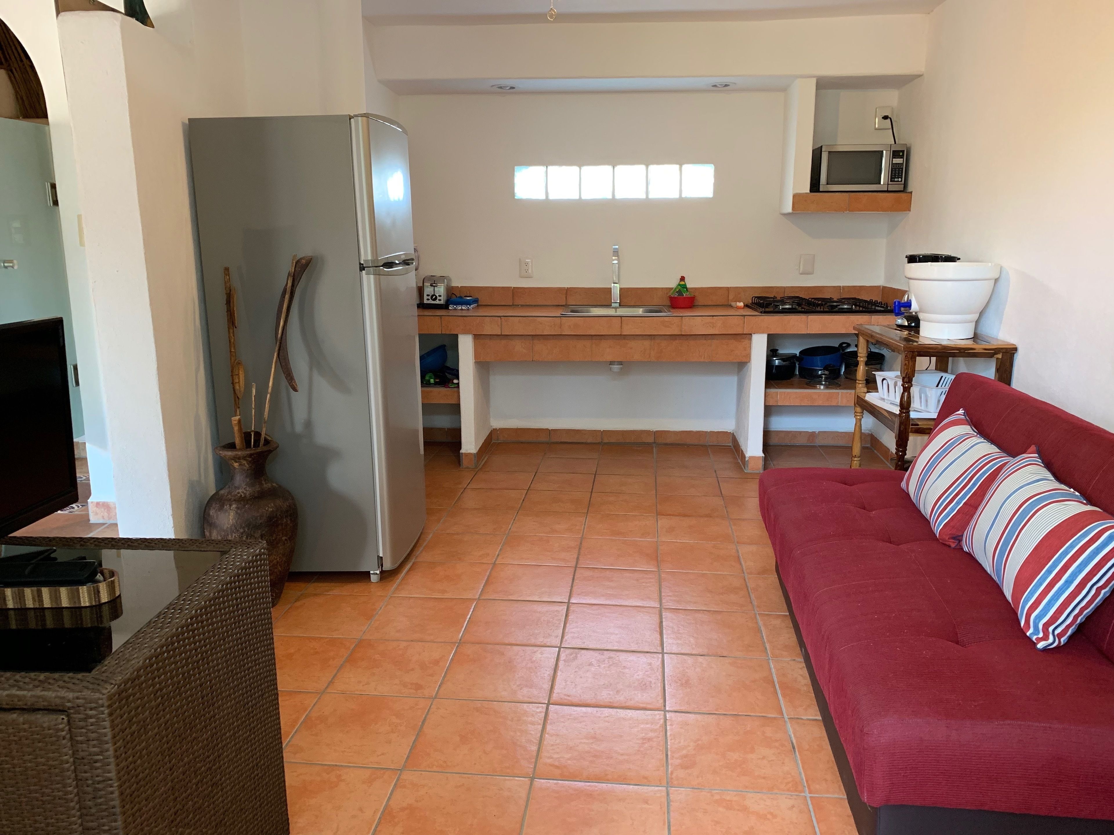 A compact kitchen with a refrigerator, microwave, and a dining area with a red sofa and striped pillow.