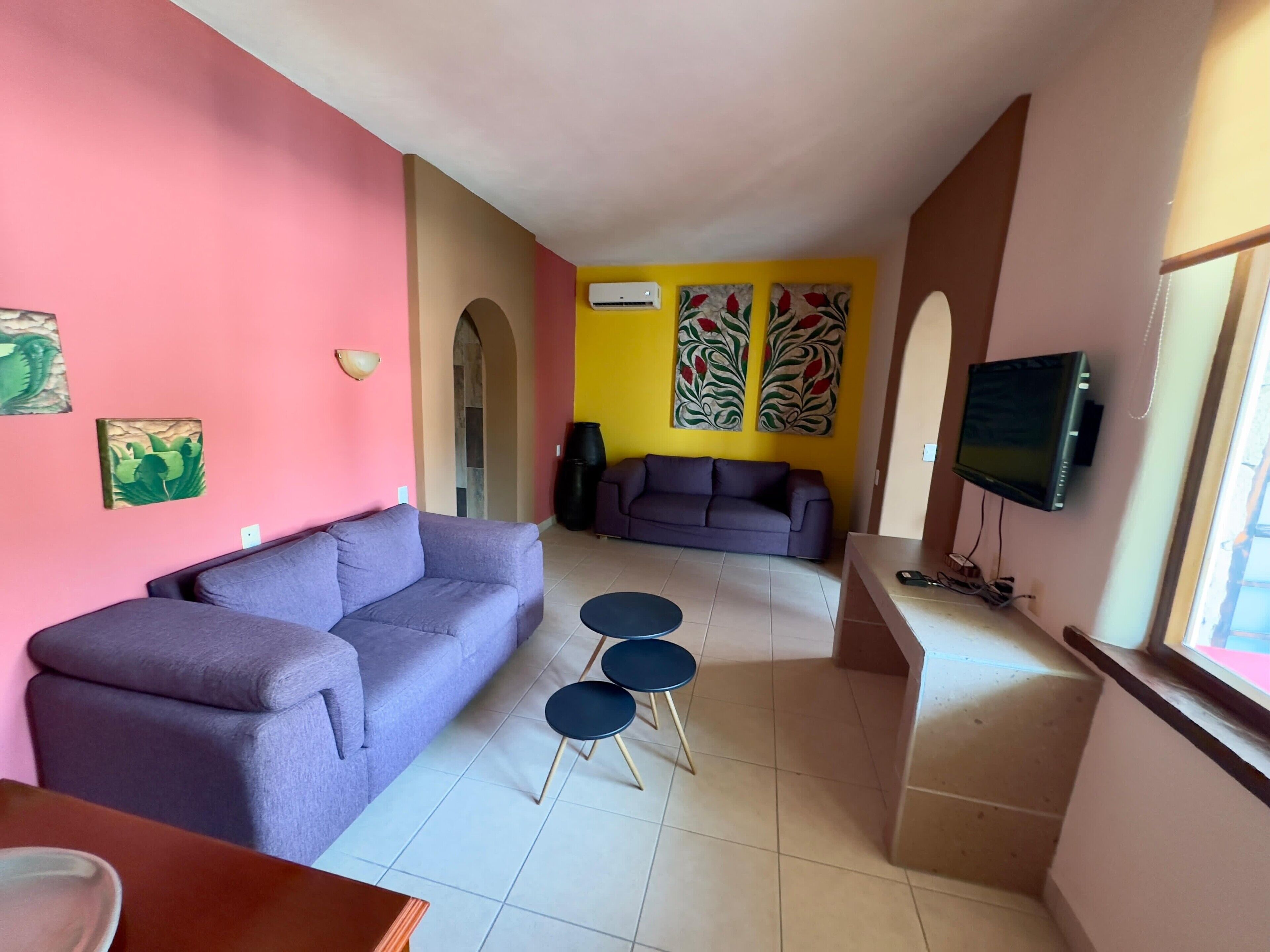 Ein Wohnzimmer mit einem violetten Sofa, einem kleinen Couchtisch und einem an der Wand befestigten Fernseher.