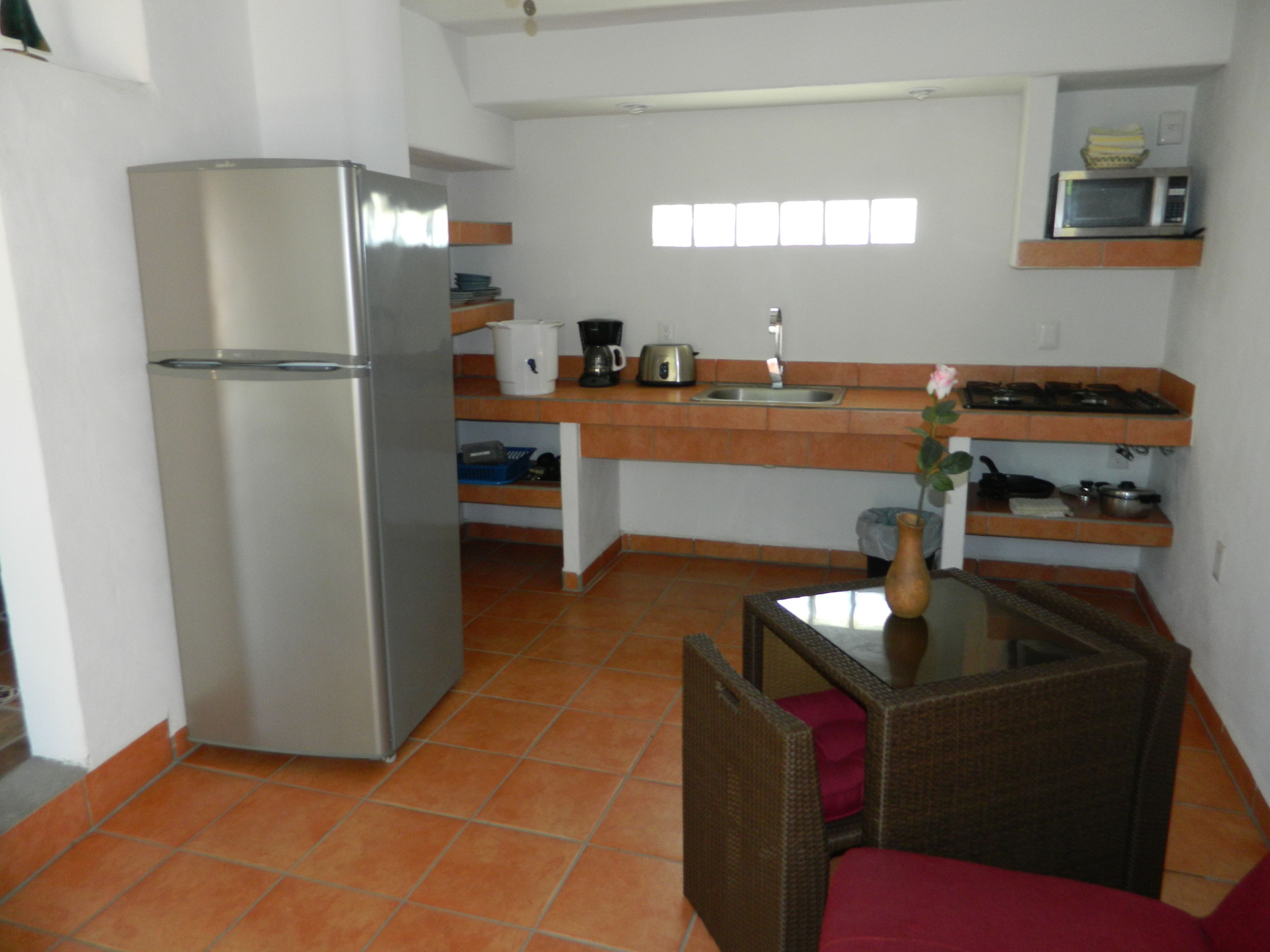 A compact kitchen with a refrigerator, a sink, and a microwave. There is a dining area with a chair and a table.