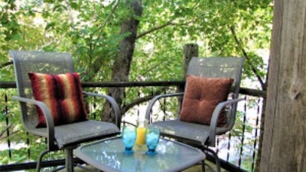 A deck with two chairs and a table, surrounded by trees. - The Olde Mill Inn Bed & Breakfast (Cumberland Gap)