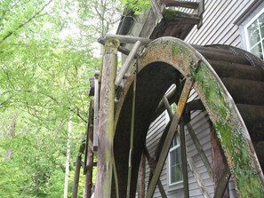 A rustic wooden structure with a metal arch, part of a building with wooden siding and a window.