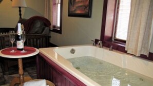 A room with a large bathtub, a small round table with a bottle of wine, and a wicker basket with a towel. - The Olde Mill Inn Bed & Breakfast (Cumberland Gap)
