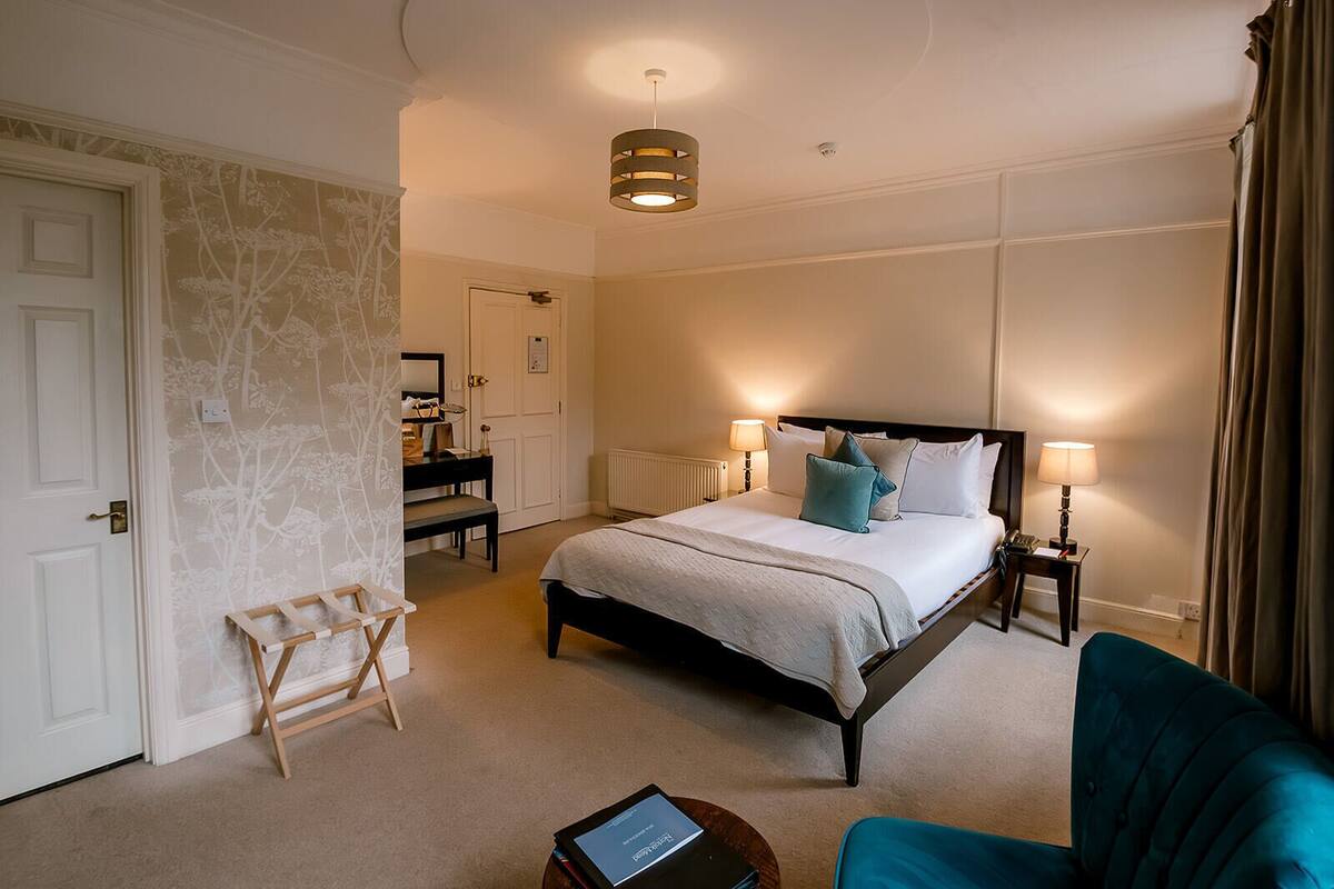 A neatly arranged bedroom with a bed, bedside lamps, a chair, and a small table.